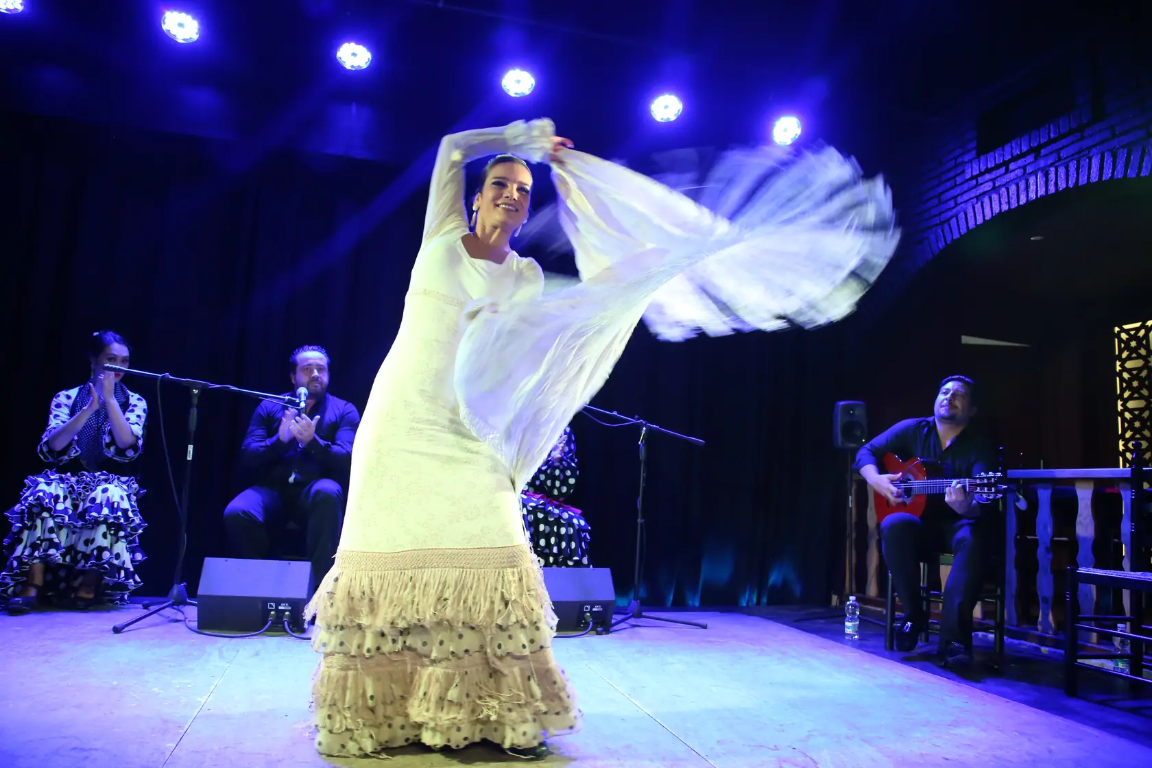 A flamenco dancer mid-performance in an intimate, warm-lit flamenco venue